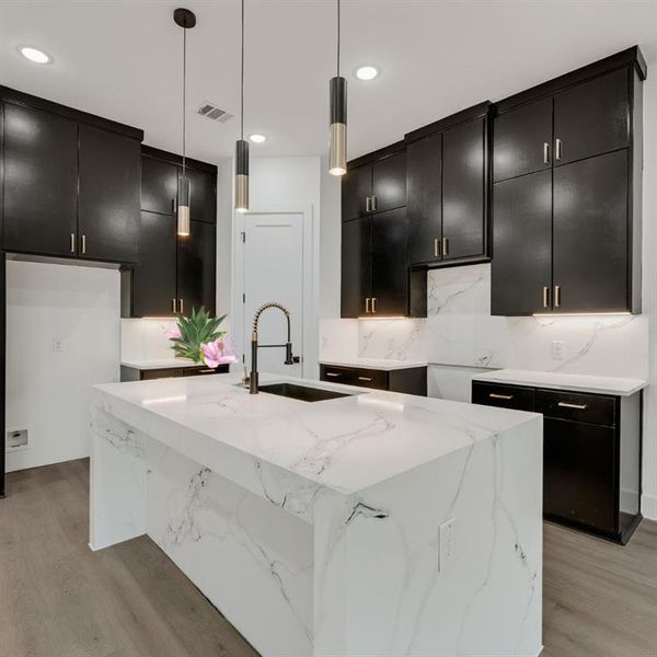 Kitchen featuring light granite countertops, dark cabinetry, decorative light fixtures, light wood-style floors, and recessed lighting