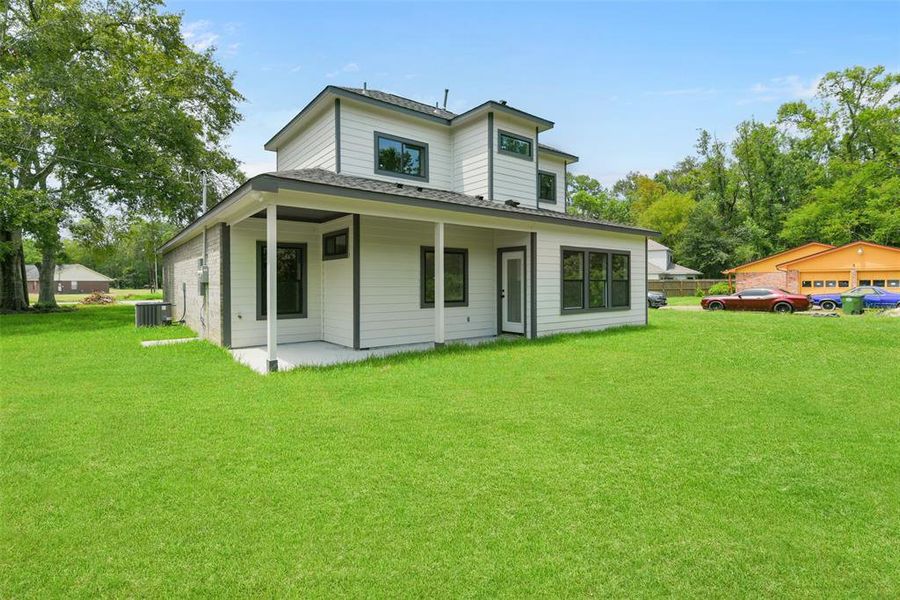 This is a  two-story home featuring a light exterior with contrasting dark trim around the windows and roofline. It has a covered porch area and is surrounded by a spacious, well-maintained lawn. The neighborhood appears peaceful with trees and other homes in the distance.