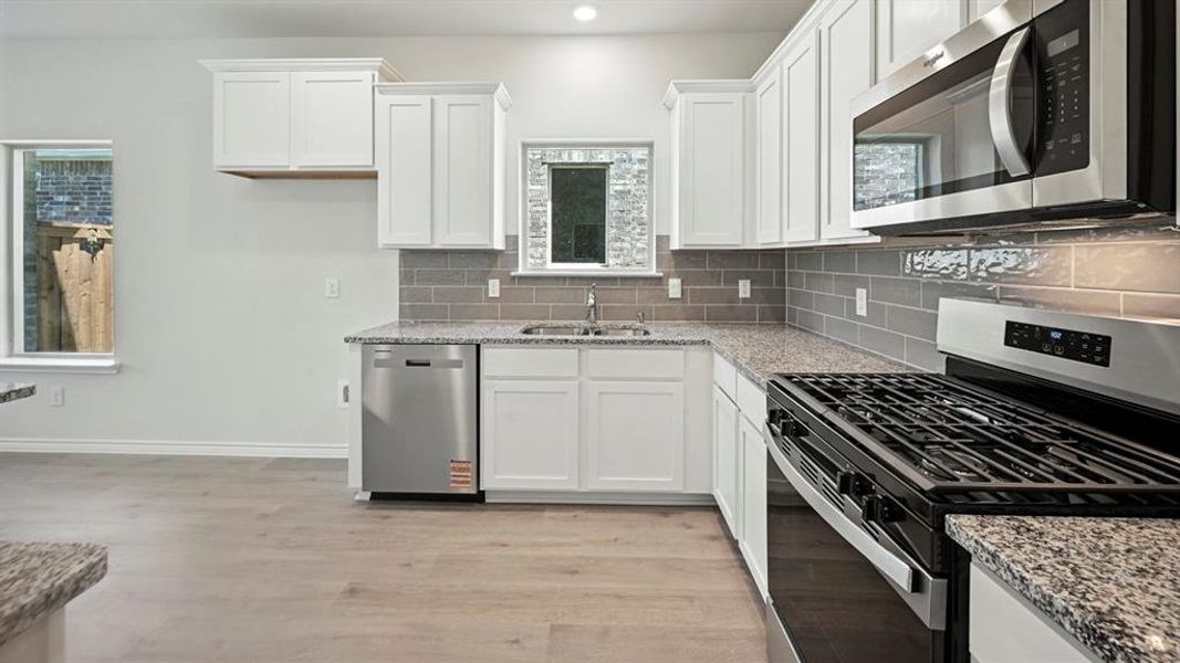 Kitchen featuring appliances with stainless steel finishes, light stone counters, white cabinetry, light wood-type flooring, and recessed lighting