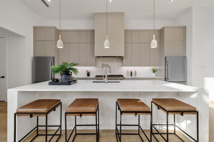 Modern kitchen featuring an extended island with waterfall countertop, integrated cooktop, ceiling-mounted range hood, stainless steel appliances, and minimalist cabinetry