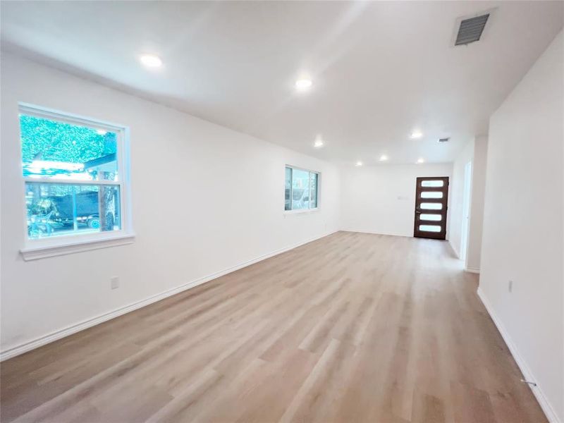 Spacious living area featuring light wood-finish flooring, recessed lighting, and white baseboards