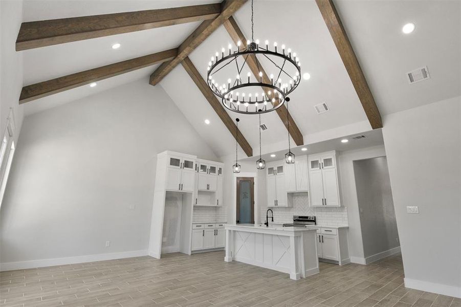 Kitchen with a center island with sink, decorative light fixtures, backsplash, white cabinetry, and light hardwood / wood-style floors