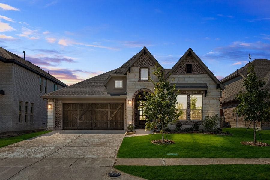 Single-story home with stone and brick exterior, wood garage door, arched entry, and manicured front lawn at dusk