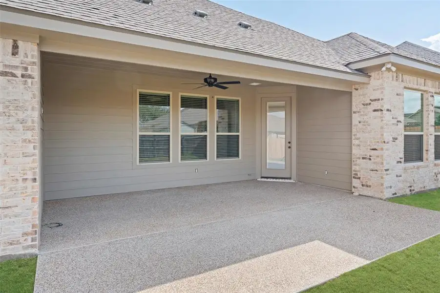 Doorway to property with ceiling fan, a patio, and roof with shingles