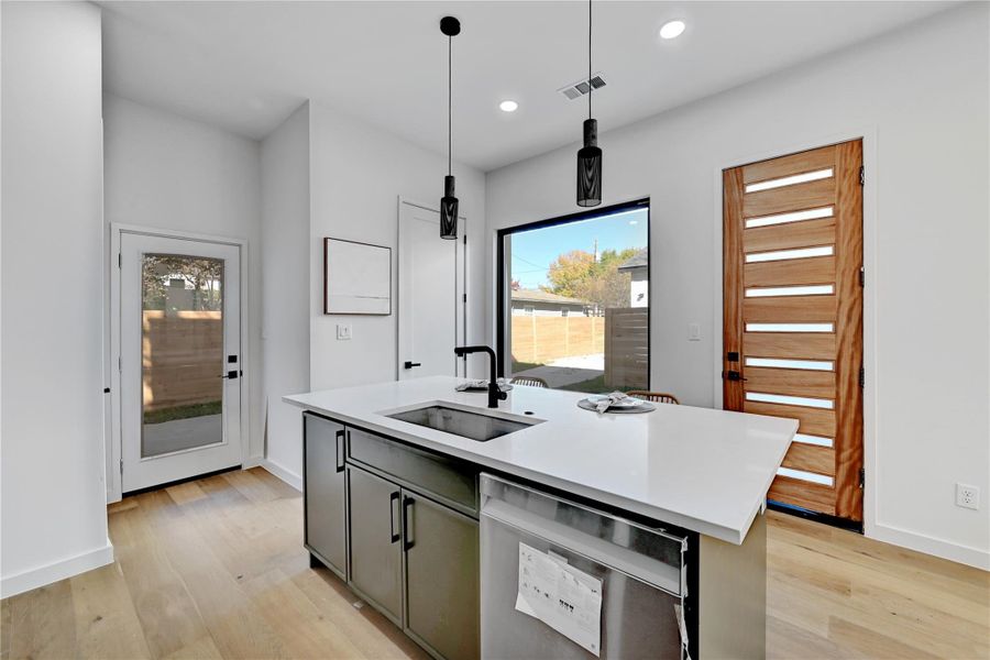 Kitchen with a center island with sink, dishwasher, hanging light fixtures, light wood-type flooring, and recessed lighting