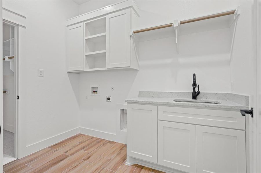 Laundry room with wood finish floors, hookup for a washing machine, hookup for an electric dryer, gas dryer hookup, and cabinet space