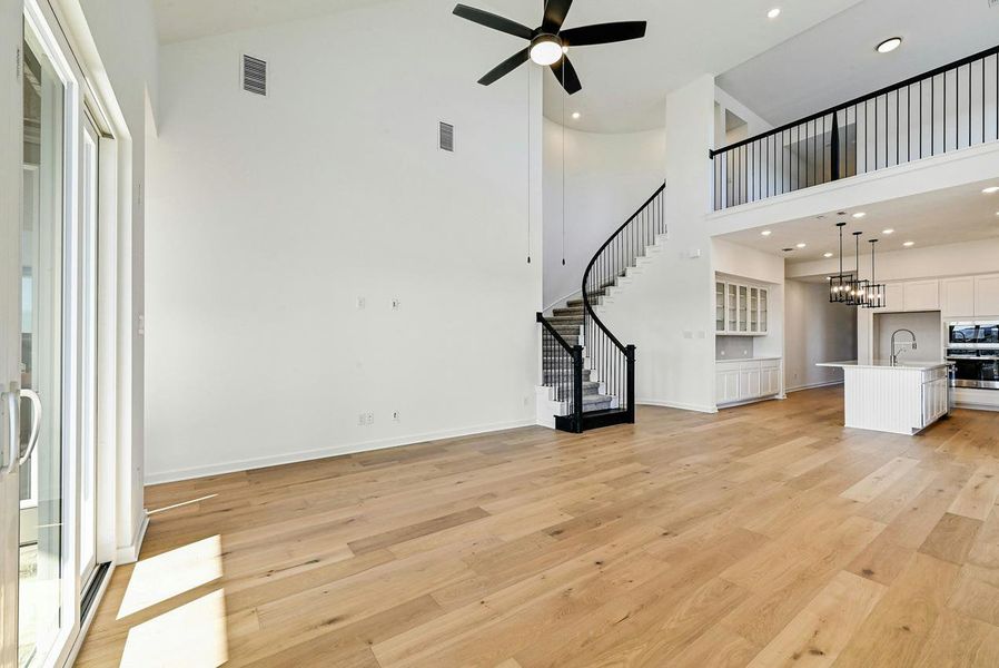 Unfurnished living room with a towering ceiling, a ceiling fan, stairway, light wood-style flooring, and recessed lighting