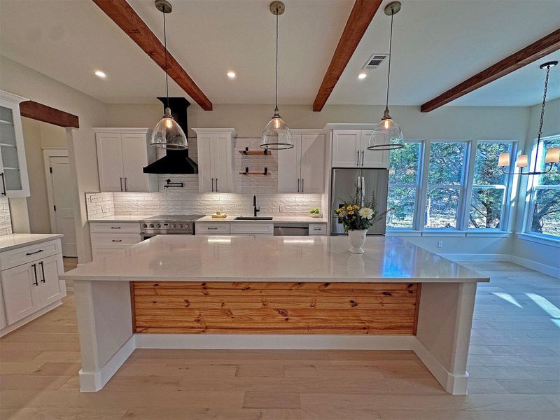 Kitchen with white cabinetry, appliances with stainless steel finishes, decorative designer light fixtures, backsplash, and solid  beam ceiling