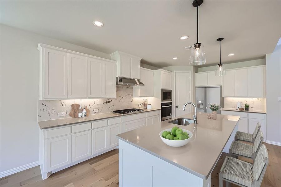 VIRTUALLY STAGED PHOTO - Kitchen featuring sink, an island with sink, appliances with stainless steel finishes, tasteful backsplash, and light hardwood / wood-style floors