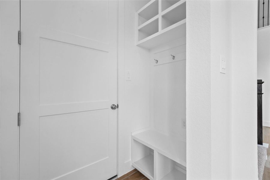 Step into this highly functional and stylish mudroom drop zone, an essential feature for a busy household. The space boasts custom-built white cabinetry and shelving, providing generous storage for coats, bags, and shoes. A comfortable built-in bench offers a convenient spot to sit, while three sleek hooks keep outerwear tidy and accessible.