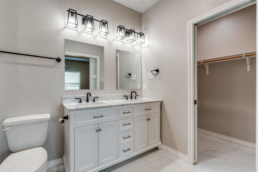 Bathroom featuring double vanity, light marble finish floors, a spacious closet, and a textured wall Bathroom featuring double vanity, light marble finish floors, a spacious closet, and a textured wall