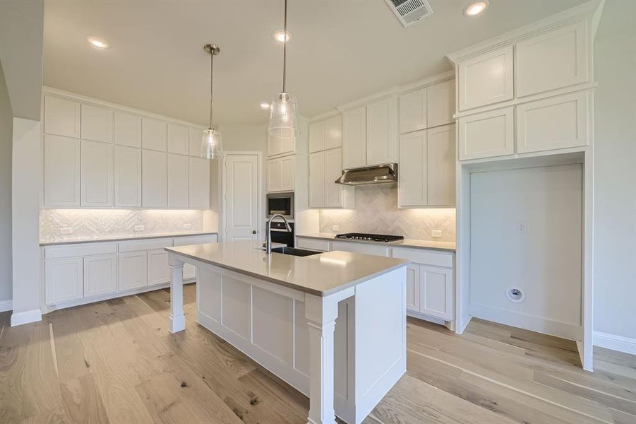 Kitchen with white cabinetry, exhaust hood, light wood-type flooring, a center island with sink, and sink