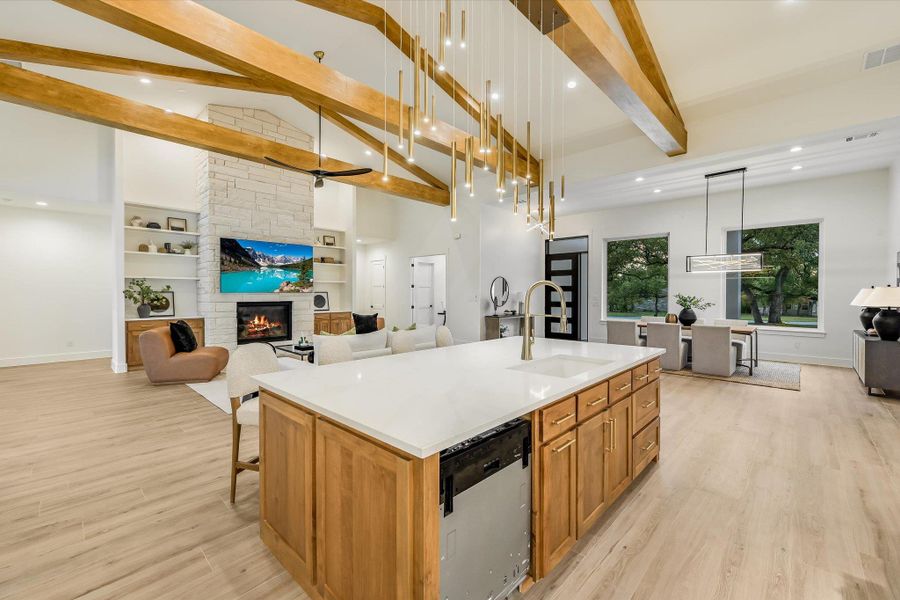 Kitchen featuring open floor plan, stainless steel dishwasher, a stone fireplace, a large island, and light stone counters