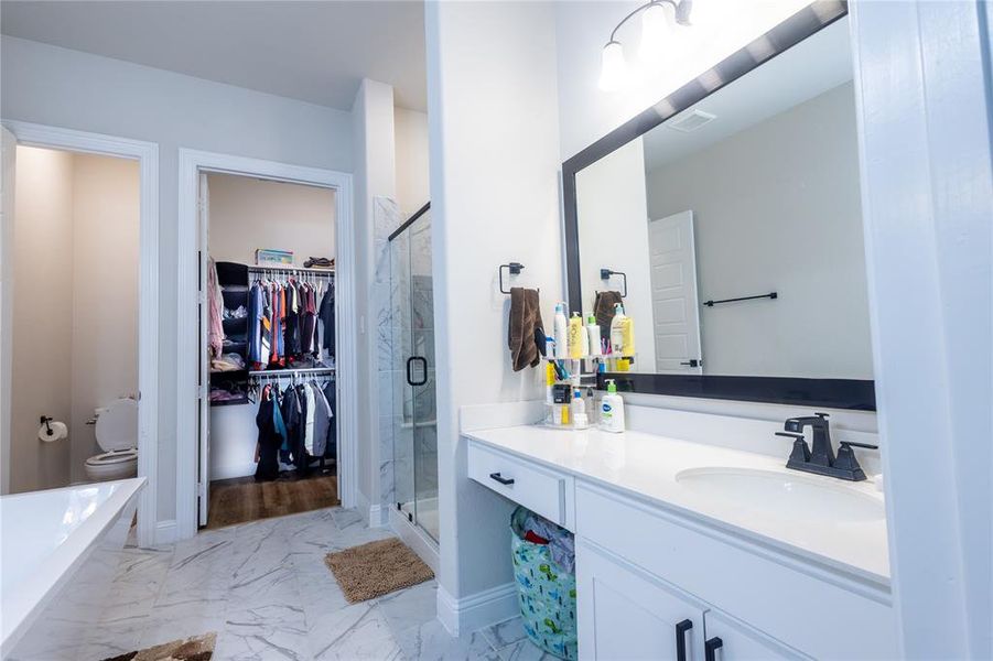 Bathroom with a walk in closet, vanity, light marble finish flooring, a stall shower, and a bath