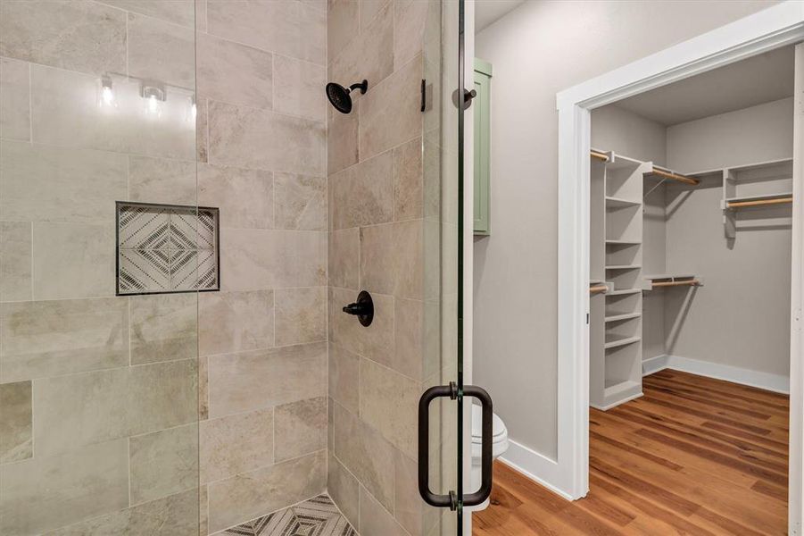 Bathroom featuring a stall shower, a walk in closet, and wood finished floors