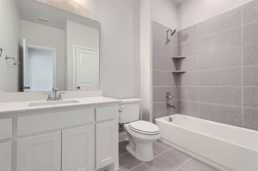 Full bathroom featuring vanity, toilet, tile patterned floors, and tiled shower / bath