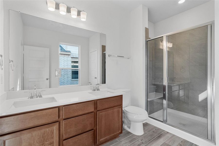 This beautifully updated primary bathroom is move-in ready! It showcases stained cabinetry paired with light countertops, dual vanity sinks, a large mirror, large walk-in shower with seat and tile surround, a linen closet, high ceilings, custom paint, and stylish modern finishes throughout.