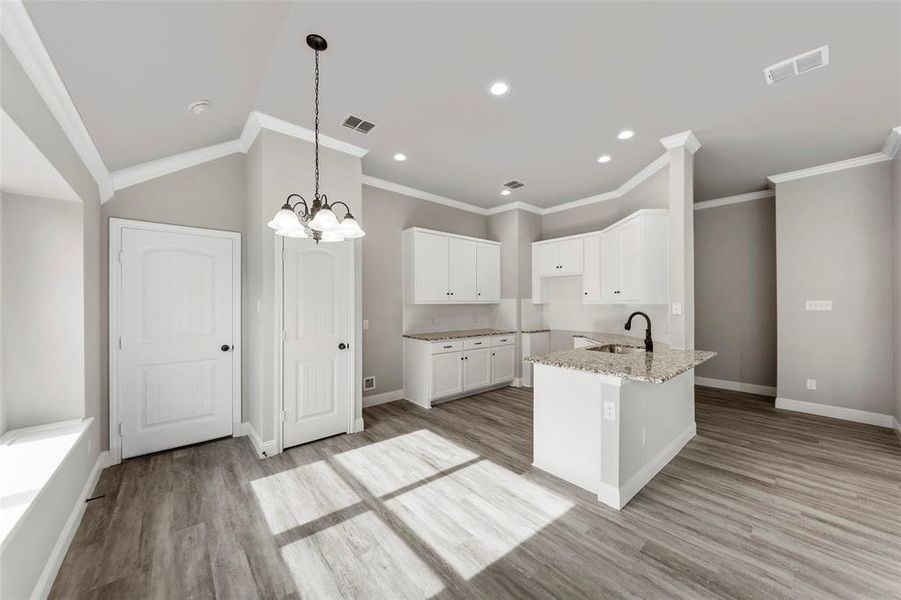 Kitchen featuring light stone counters, a notable chandelier, light hardwood / wood-style floors, white cabinets, and ornamental molding