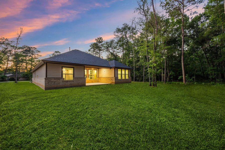 Spacious covered patio with brick and siding walls, recessed lighting, and a ceiling fan, perfect for outdoor relaxation or entertaining. Large windows offer a view into the home, and the surrounding greenery adds a touch of nature.