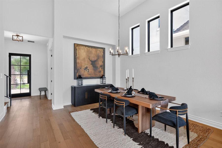 Elegant dining space featuring high ceilings, a chic chandelier, and rich hardwood flooring. Elegant dining space featuring high ceilings, a chic chandelier, and rich hardwood flooring.