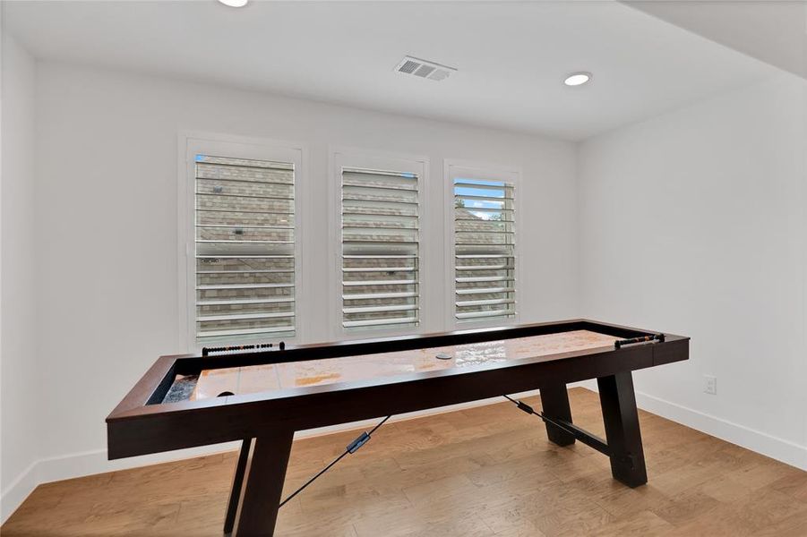 Bright room featuring three windows with plantation shutters, recessed lighting, and wood-finish flooring