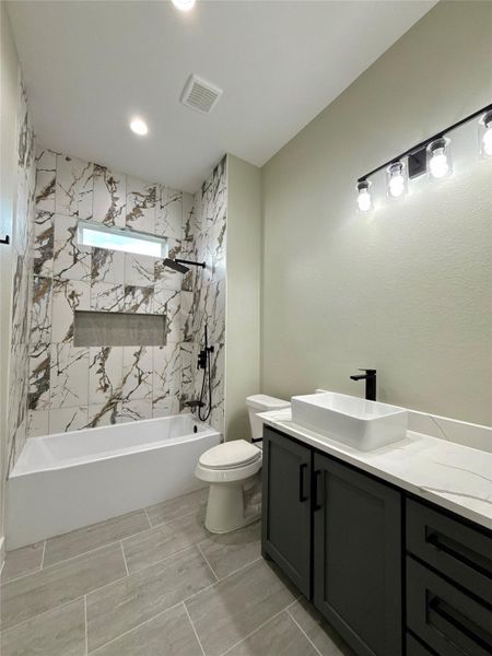 This modern bathroom features a sleek design with a quartz-tiled shower and bathtub, a stylish dark vanity with a vessel sink, and contemporary lighting. The neutral tones and clean lines create a luxurious and inviting space.