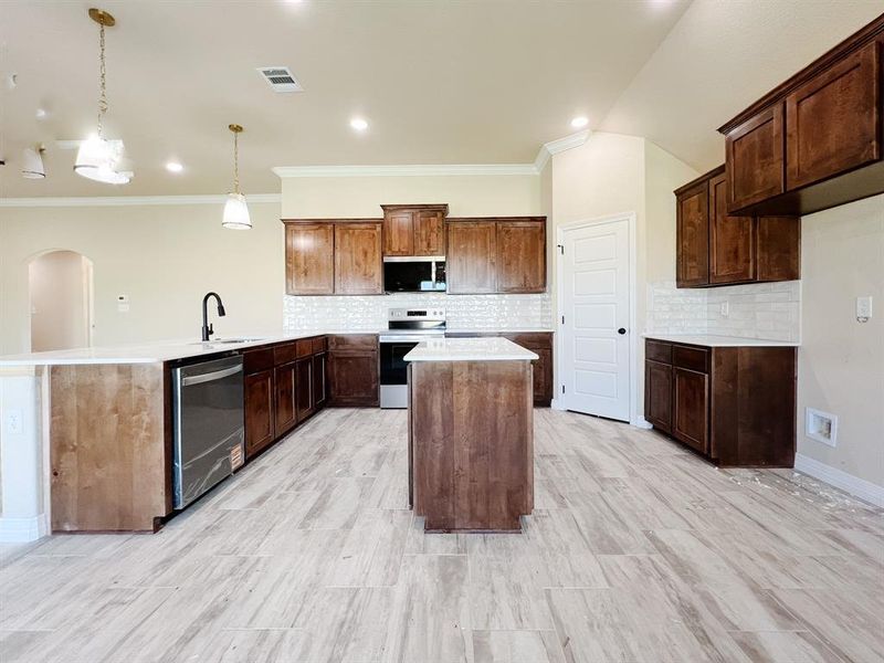 Kitchen with tasteful backsplash, a kitchen island, arched walkways, hanging light fixtures, and ornamental molding Kitchen with tasteful backsplash, a kitchen island, arched walkways, hanging light fixtures, and ornamental molding