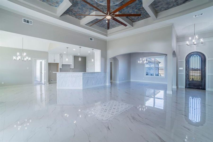 Unfurnished living room with a chandelier, coffered ceiling, a high ceiling, light marble finish floors, and arched walkways