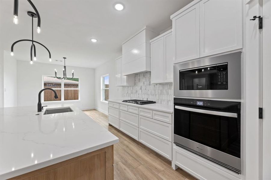 Kitchen featuring stainless steel appliances, decorative light fixtures, backsplash, sink, and white cabinetry