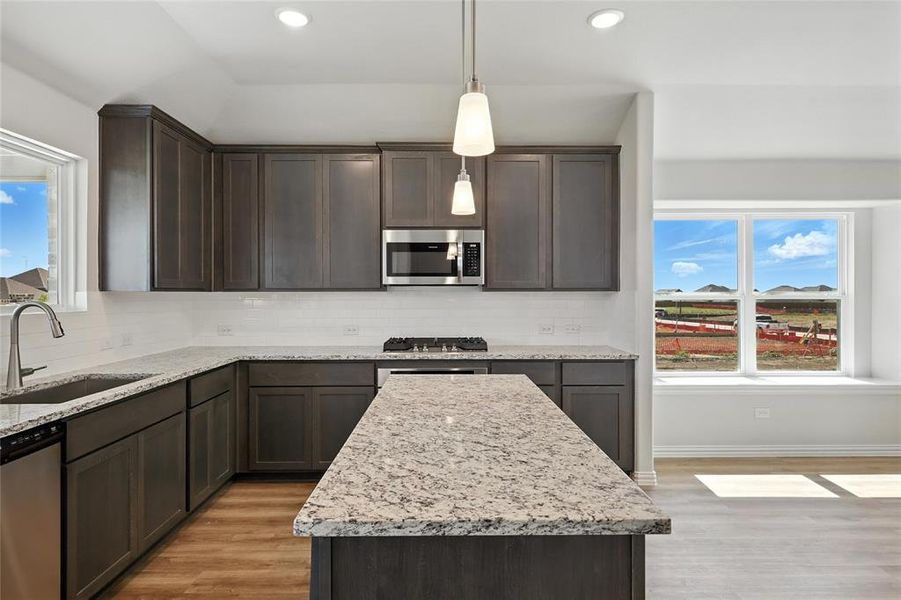 Kitchen with appliances with stainless steel finishes, light wood-style floors, dark brown cabinets, decorative backsplash, and recessed lighting Kitchen with appliances with stainless steel finishes, light wood-style floors, dark brown cabinets, decorative backsplash, and recessed lighting