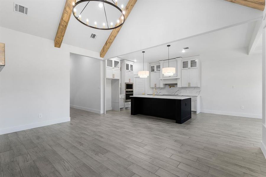 Kitchen with white cabinetry, backsplash, decorative light fixtures, a center island with sink, and appliances with stainless steel finishes