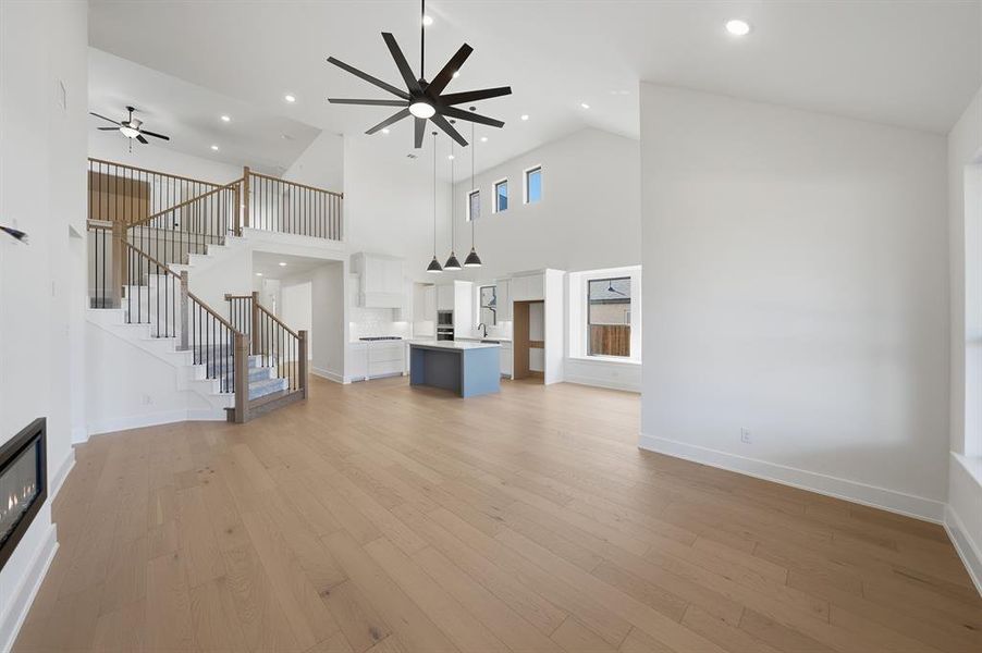 Unfurnished living room with light wood-type flooring, stairs, a glass covered fireplace, a ceiling fan, and recessed lighting Unfurnished living room with light wood-type flooring, stairs, a glass covered fireplace, a ceiling fan, and recessed lighting