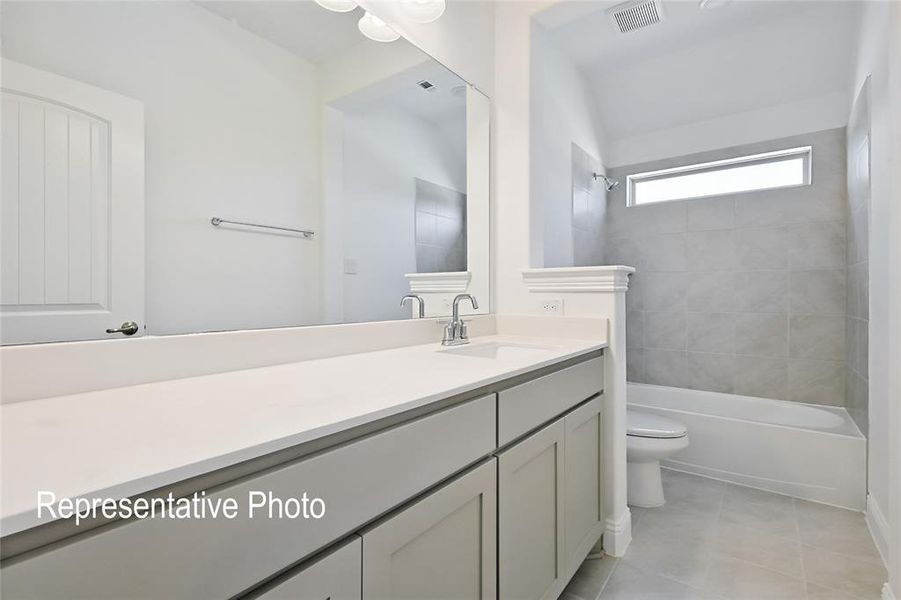 Bathroom featuring a light gray vanity with white countertop, chrome fixtures, a full-width mirror, and a tub-shower combination with gray tile surround and a horizontal window