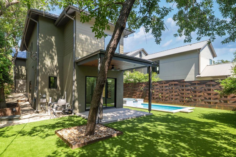 Expansive green space featuring a geometric pool, integrated spa, and an outdoor patio with a built-in ceiling fan