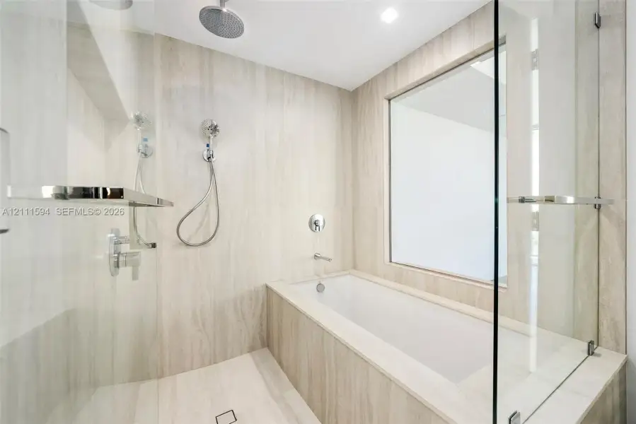 Wet room featuring stone-finish wall and floor tiling, deep-soaking bathtub, glass partition, wall-mounted shower system with rain head, and integrated shelving Wet room featuring stone-finish wall and floor tiling, deep-soaking bathtub, glass partition, wall-mounted shower system with rain head, and integrated shelving