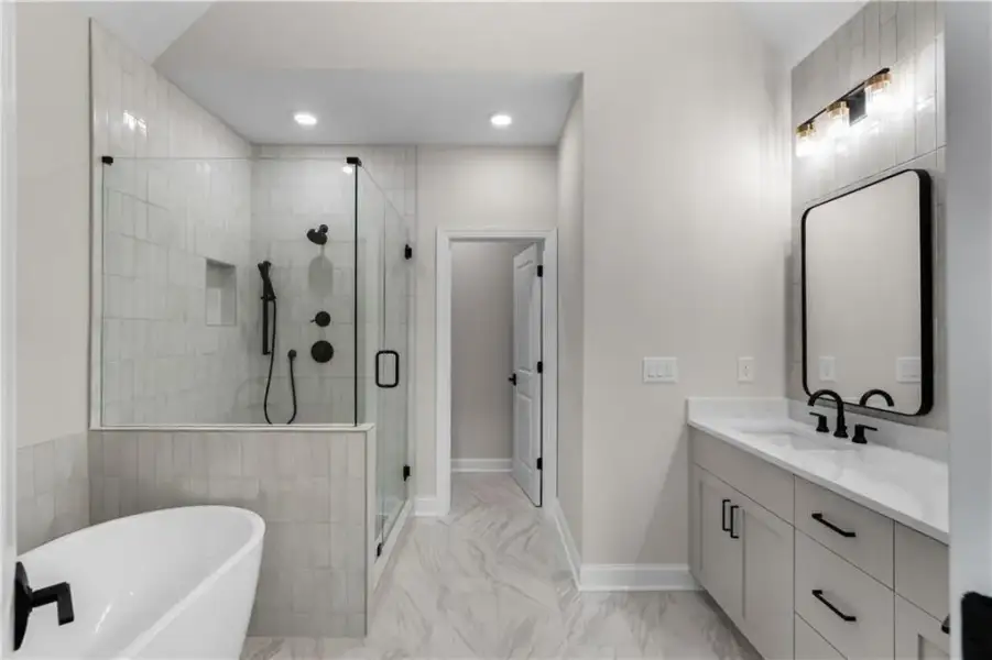 Spacious bathroom featuring a freestanding tub, glass-enclosed shower, single vanity with light countertop, and a large mirror with integrated lighting.  THE VAULTED CEILING CREATES DRAMATIC VOLUME