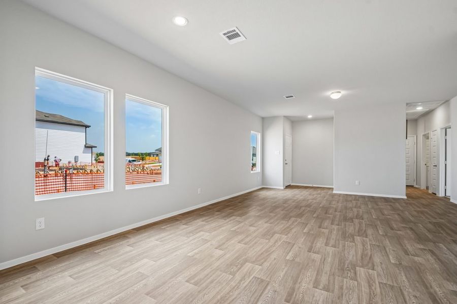 Image of home living room looking towards the front door on the left and hallway to bedrooms on the right. Wood-look flooring, white walls and doors, and two windows on the left
