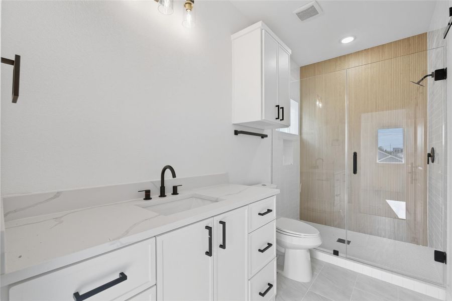 The private ensuite bath combines comfort with modern finishes, featuring a spacious walk-in shower with glass doors and custom tile. A sleek vanity with quartz countertops, matte black fixtures, and ample storage makes the space as practical as it is stylish. Thoughtful details and clean design turn this bathroom into the perfect relaxing space! The private ensuite bath combines comfort with modern finishes, featuring a spacious walk-in shower with glass doors and custom tile. A sleek vanity with quartz countertops, matte black fixtures, and ample storage makes the space as practical as it is stylish. Thoughtful details and clean design turn this bathroom into the perfect relaxing space!
