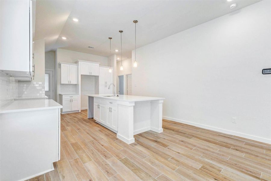 Open kitchen and dining area featuring wood-look tile flooring, white cabinetry, quartz countertops, pendant lighting, and a large center island. The spacious layout offers room for dining, gathering, and everyday meal prep.