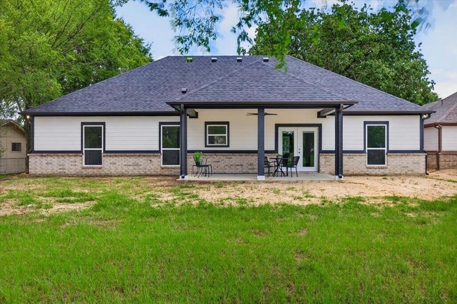 Rear elevation featuring a covered concrete patio with dark columns and dual glass panel doors.