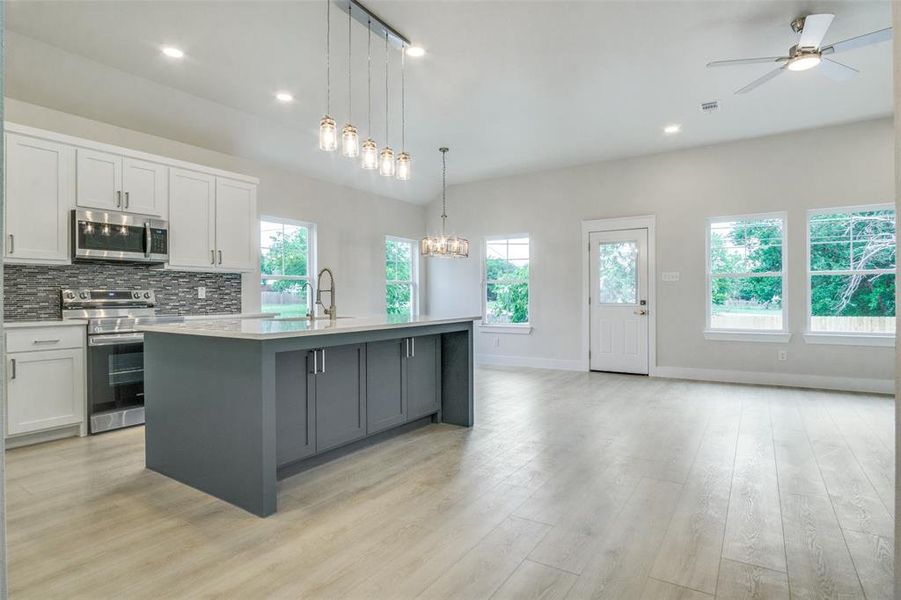 Kitchen featuring backsplash, light countertops, a sink, ceiling fan with notable chandelier, and stainless steel appliances