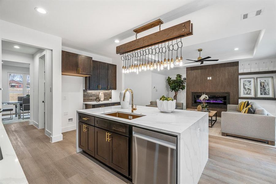 Kitchen with light hardwood / wood-style flooring, an island with sink, a large fireplace, sink, and ceiling fan