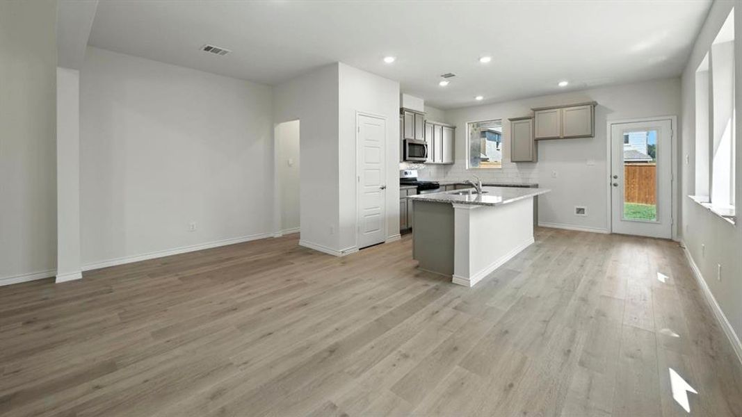 Kitchen featuring gray cabinets, a center island with sink, backsplash, appliances with stainless steel finishes, and recessed lighting