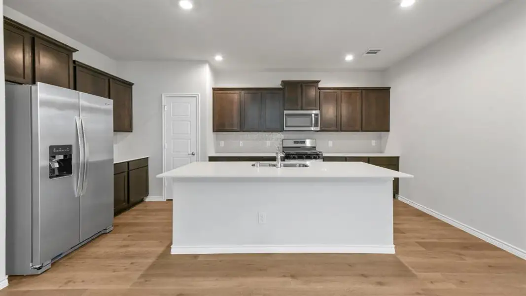 Kitchen featuring stainless steel appliances, a center island with sink, recessed lighting, light wood-type flooring, and dark wood finish cabinetry Kitchen featuring stainless steel appliances, a center island with sink, recessed lighting, light wood-type flooring, and dark wood finish cabinetry