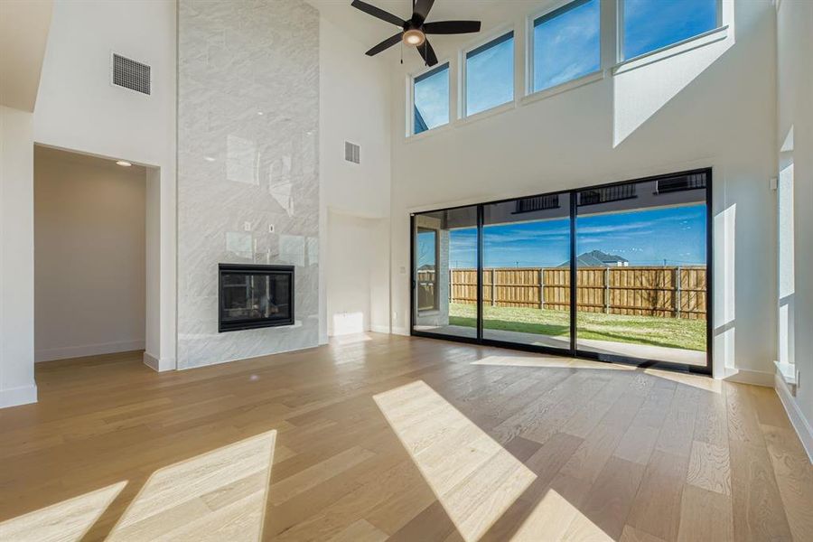 Unfurnished living room with light wood finished floors, a high end fireplace, a ceiling fan, and a high ceiling Unfurnished living room with light wood finished floors, a high end fireplace, a ceiling fan, and a high ceiling