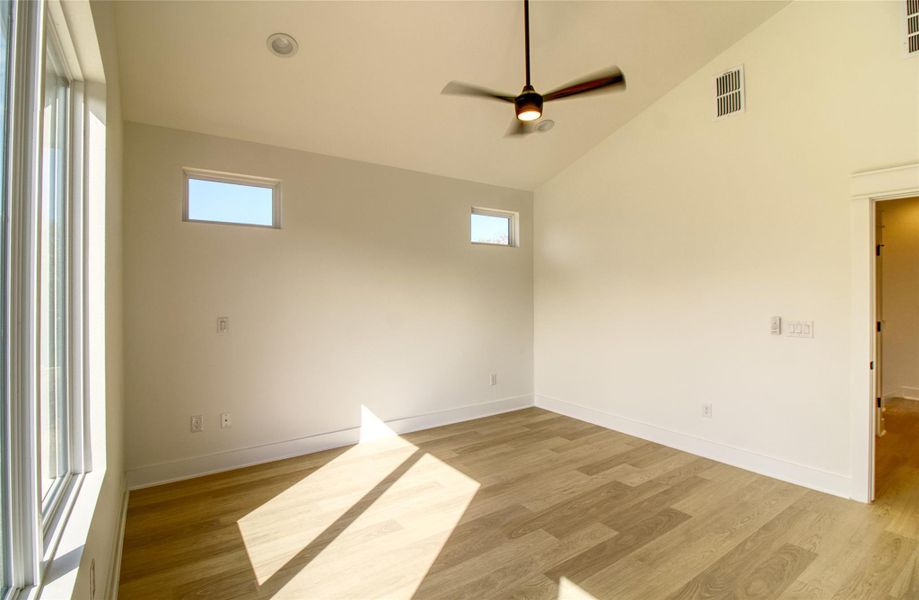 Spare room featuring healthy amount of natural light, a ceiling fan, light wood-style flooring, and high vaulted ceiling