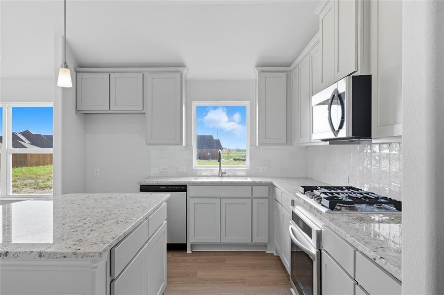 Kitchen featuring tasteful backsplash, light wood-style flooring, and light stone counters Kitchen featuring tasteful backsplash, light wood-style flooring, and light stone counters