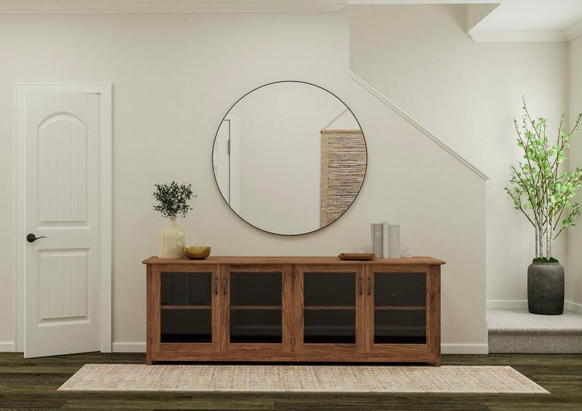 Rendering of the entryway in the home
  with vinyl plank flooring. The space is decorated with a buffet, rug and
  large round mirror. The bottom of the staircase, entrance to the living room
  and the doorway to the powder room are visible.