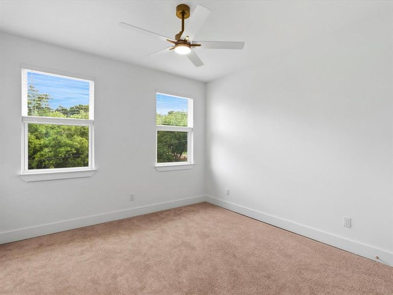 Bright interior space with two double-hung windows, plush brown carpeting, and a modern ceiling fan with a brass-finish fixture