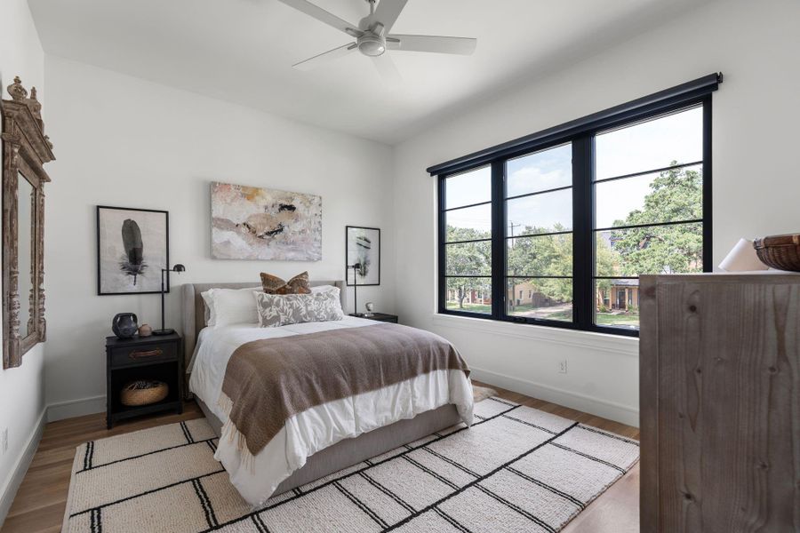 The secondary bedroom #1 features hardwood flooring, a ceiling fan, and oversized black framed windows that fill the space with natural light.